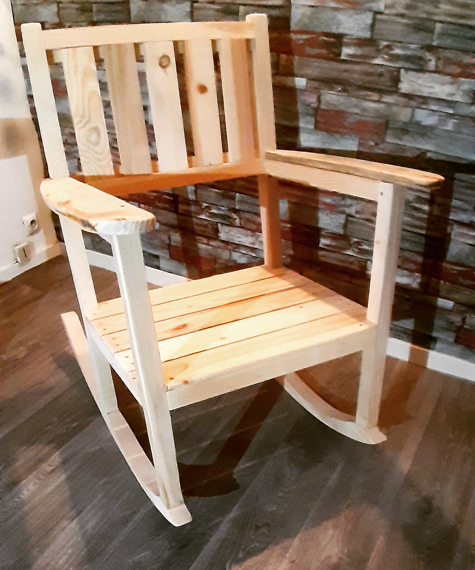 Rocking-chair en pin clair, en bois de récupération, devant un mur de pierre