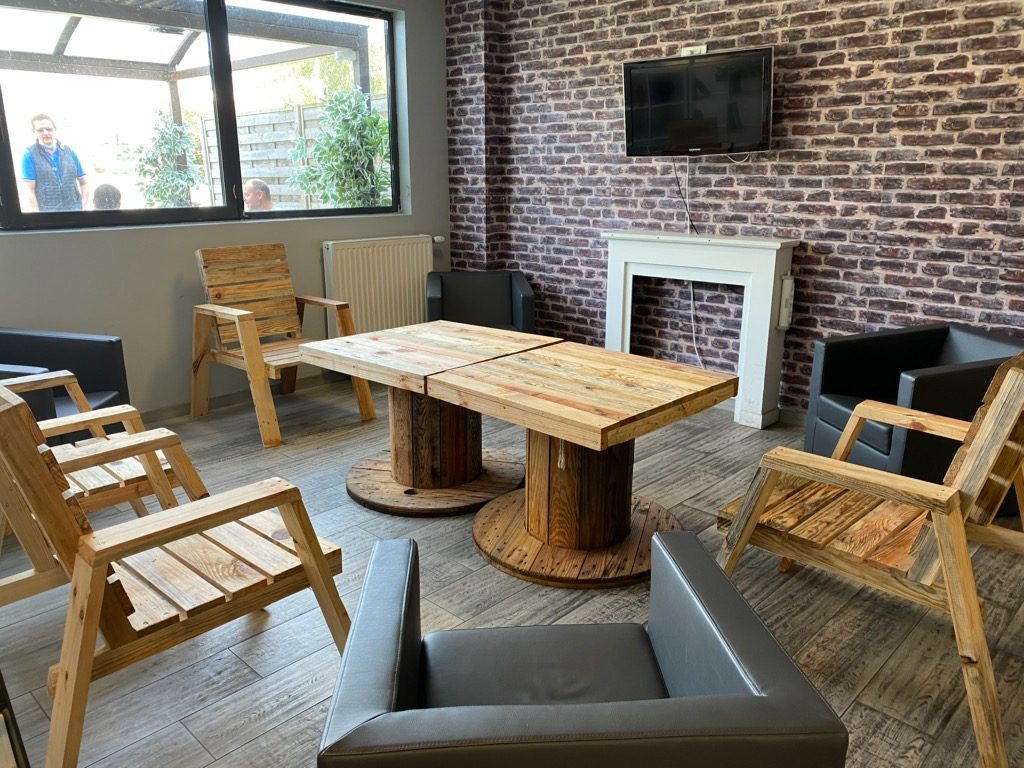 Salon monté par l'atelier : fauteuils en bois de palette et table touret devant une cheminée et un mur de briques