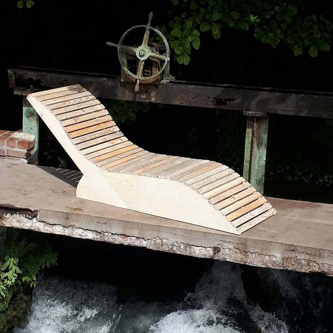 Bain de soleil en bois de récupération posé sur le pont d'un moulin, au-dessus de l'eau